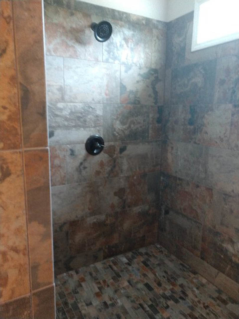 Walk-in shower with marble tile floor, tiled walls, and a white rectangular window letting in natural light