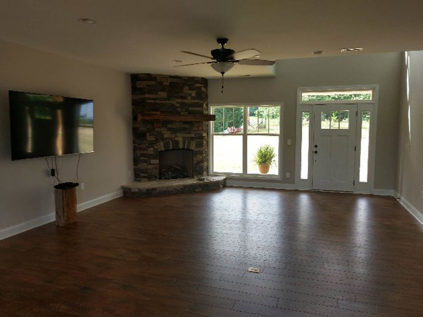Living room with wood flooring, stone fireplace, ceiling fan, white door with glass panes, potted plant, and natural light