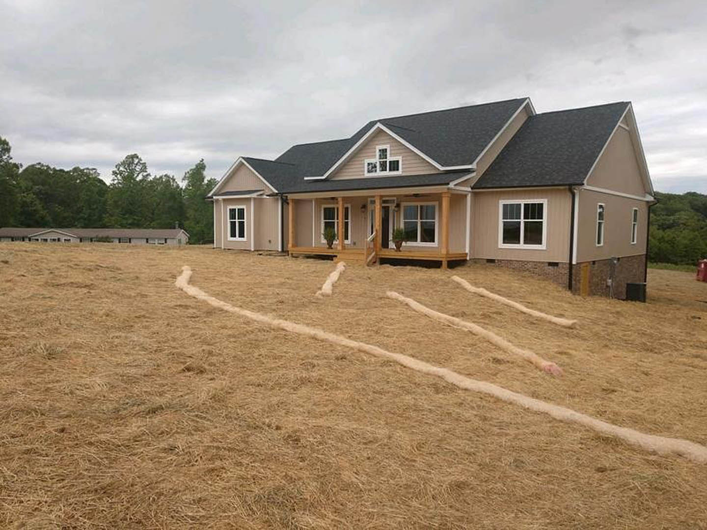 Two-story cottage-style home with gray siding, covered front porch, large grassy yard, mature trees, and white-framed windows.