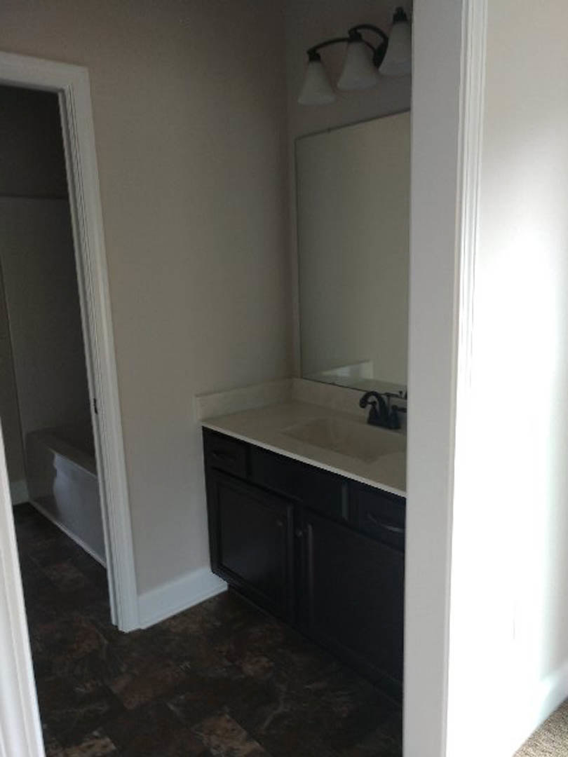 White bathroom countertop with black drawer, rectangular sink, chrome faucet, large wall mirror, light gray tile backsplash, and neutral painted walls