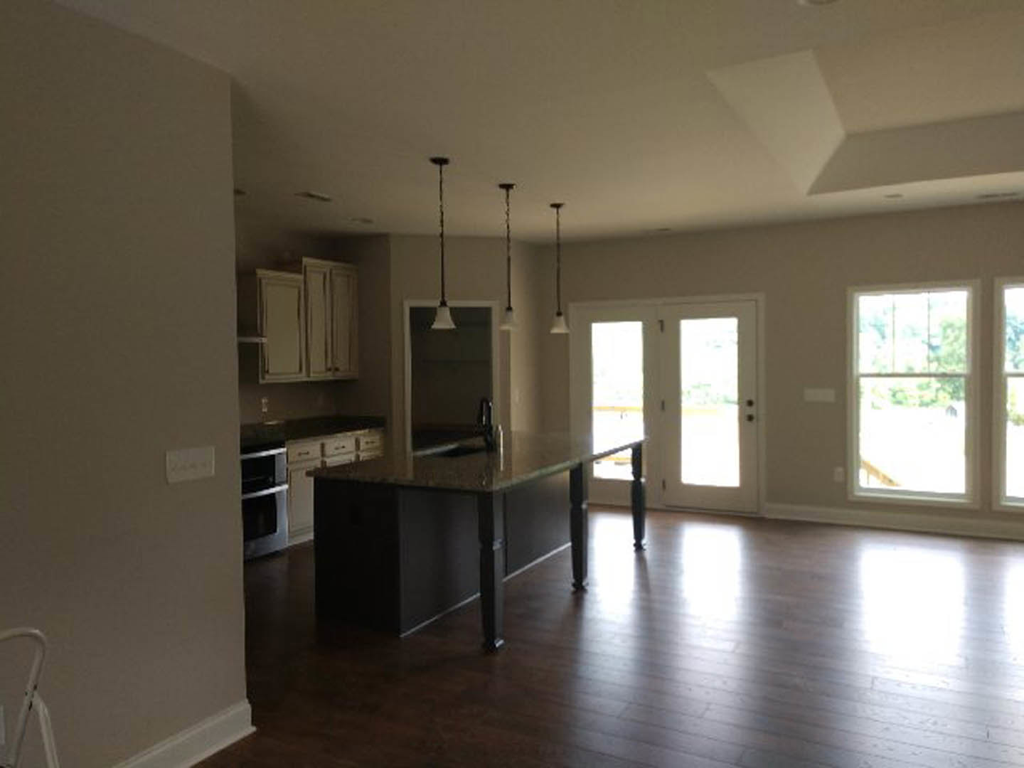 Kitchen with marble-topped island, wood flooring, white cabinetry, stainless steel appliances, double glass doors, and window with white frame