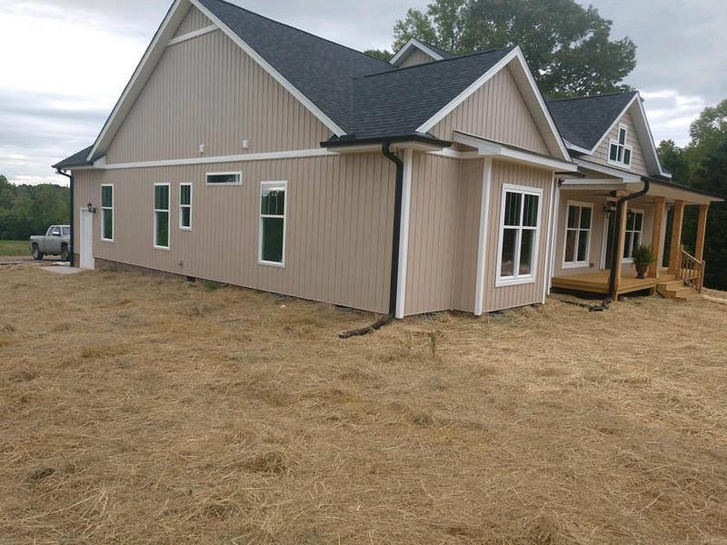Two-story home with gray siding, white trim, covered front porch, elevated wooden deck, and landscaped yard with mature trees; white-framed windows and visible gutter along