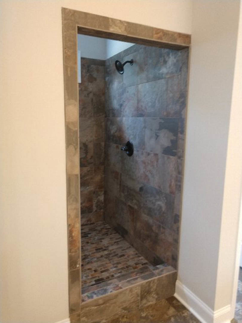 Walk-in shower with light gray marble tile floor, plaster walls, and glass door