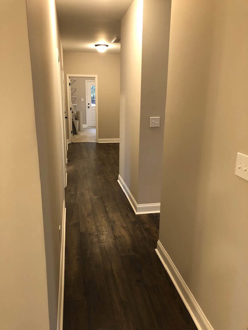 Hallway with dark wood flooring, white trim, white walls, a white door with black handles, and a ceiling light fixture
