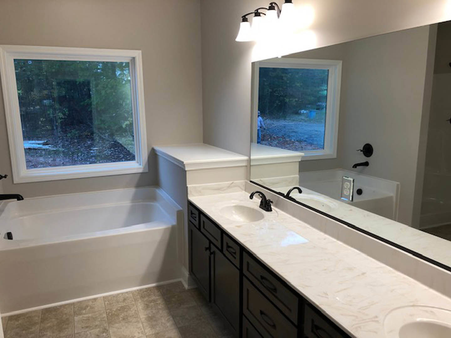 Bathroom with a wide mirror above a white countertop, modern sink, freestanding tub, tiled walls, and multi-bulb light fixture