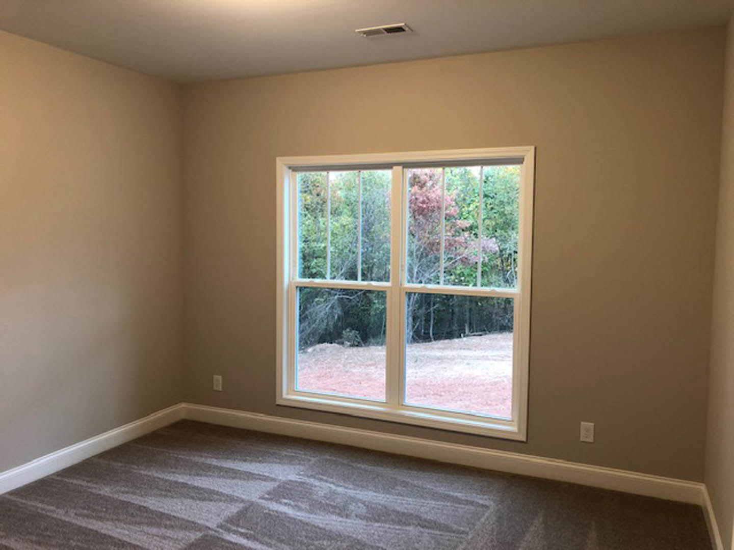 Carpeted bedroom with large window, white walls, ceiling vent, and window blinds; trees visible outside