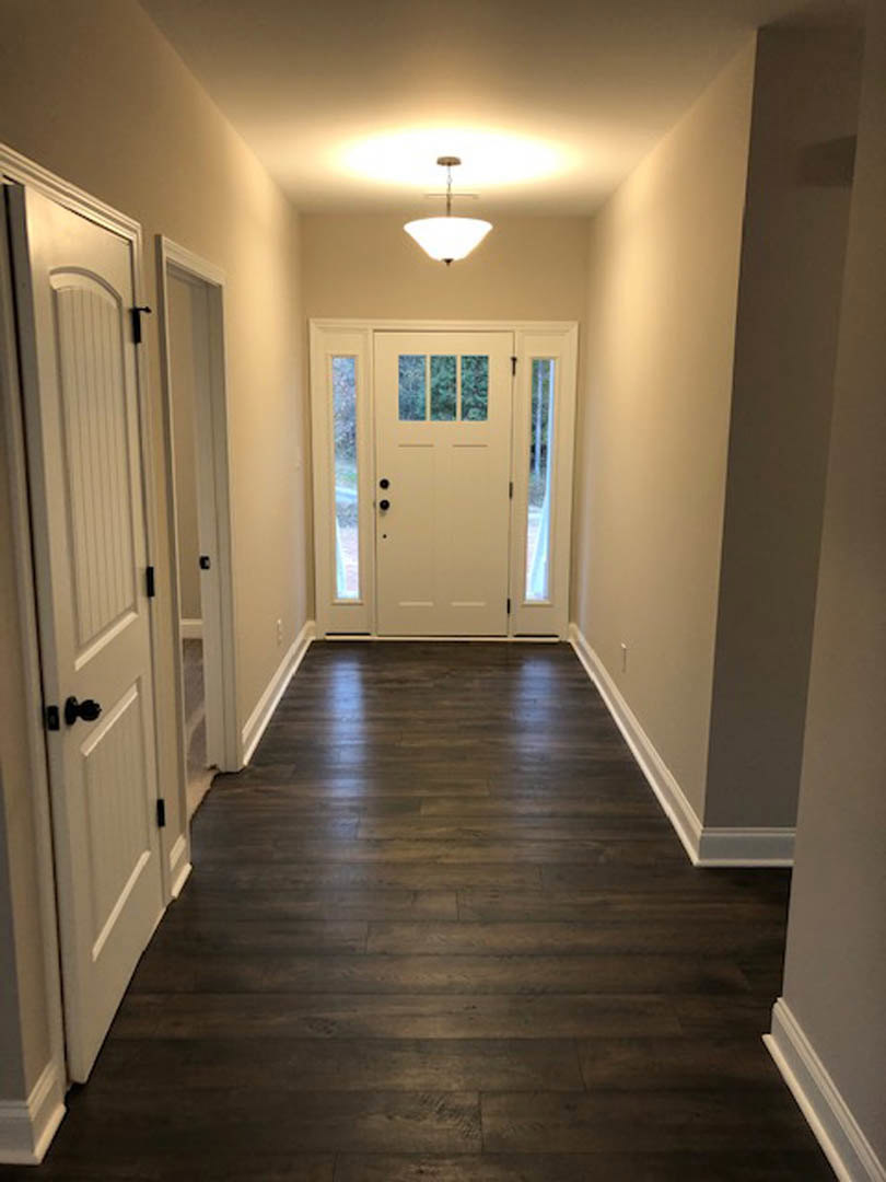 Hallway with dark wood flooring, white door featuring glass window panes, white plaster walls, and ceiling light fixture