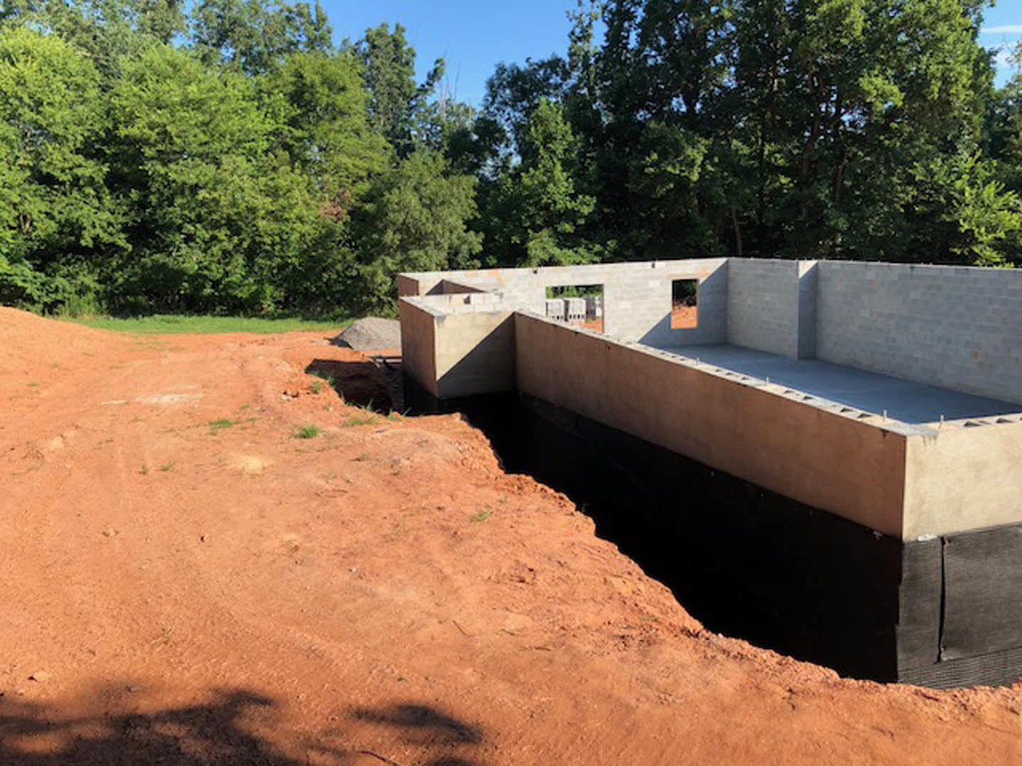 Concrete foundation with exposed soil and central hole, surrounded by trees and blue sky in the background