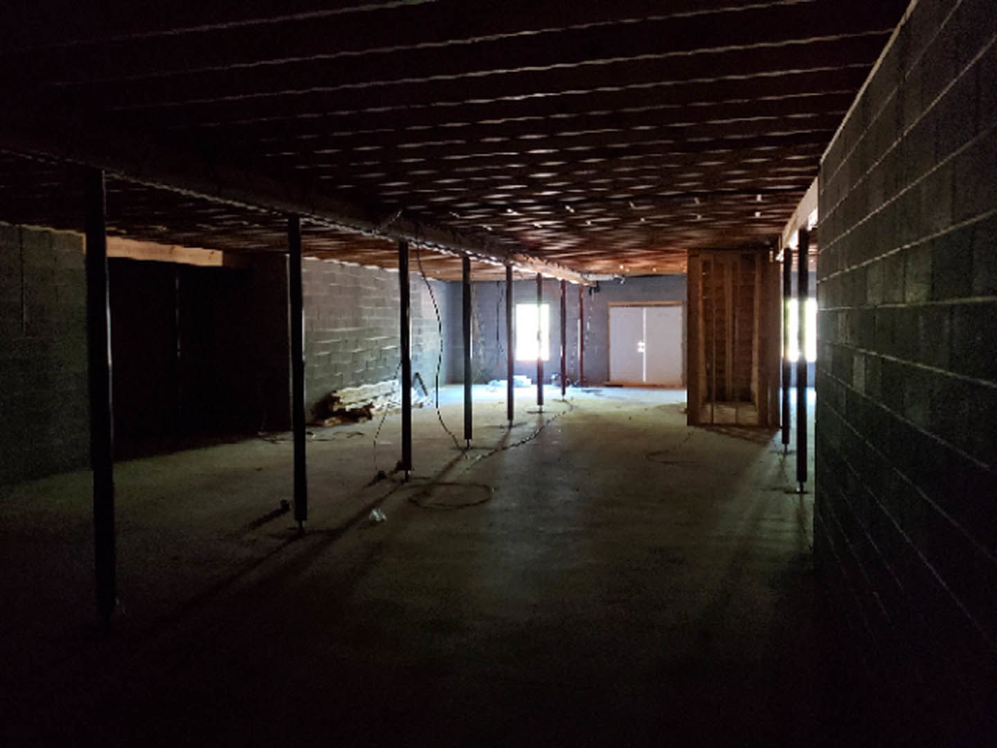 Dark interior with exposed brick walls, wood shelving, white door illuminated by light, and black ceiling