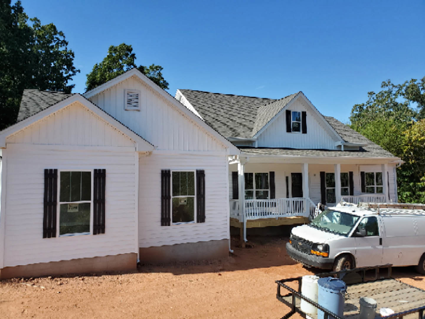 White two-story house with large windows, front porch, and a white van parked on the driveway; blue sky and landscaping visible.