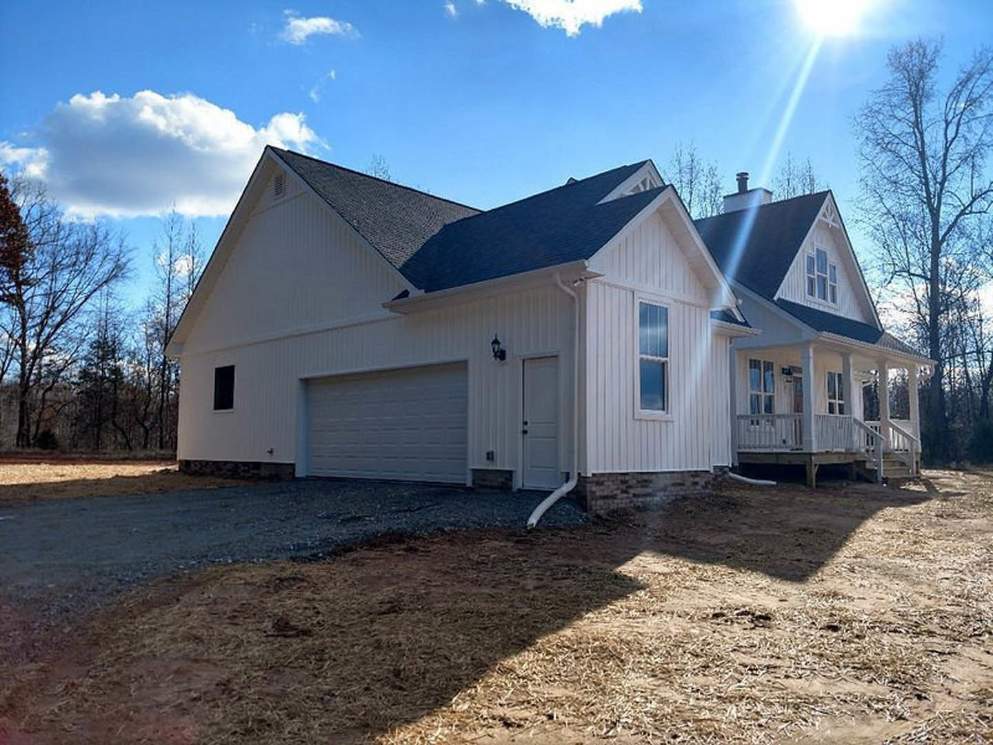 Two-story home with attached garage, concrete driveway, white garage door, white-framed windows, white exterior pipe, and surrounding trees under partly cloudy sky