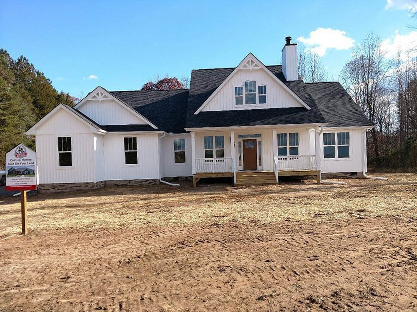 White house with black roof and brown door, dirt yard in foreground, Robert Frost Farm visible in background, trees and cloudy sky.