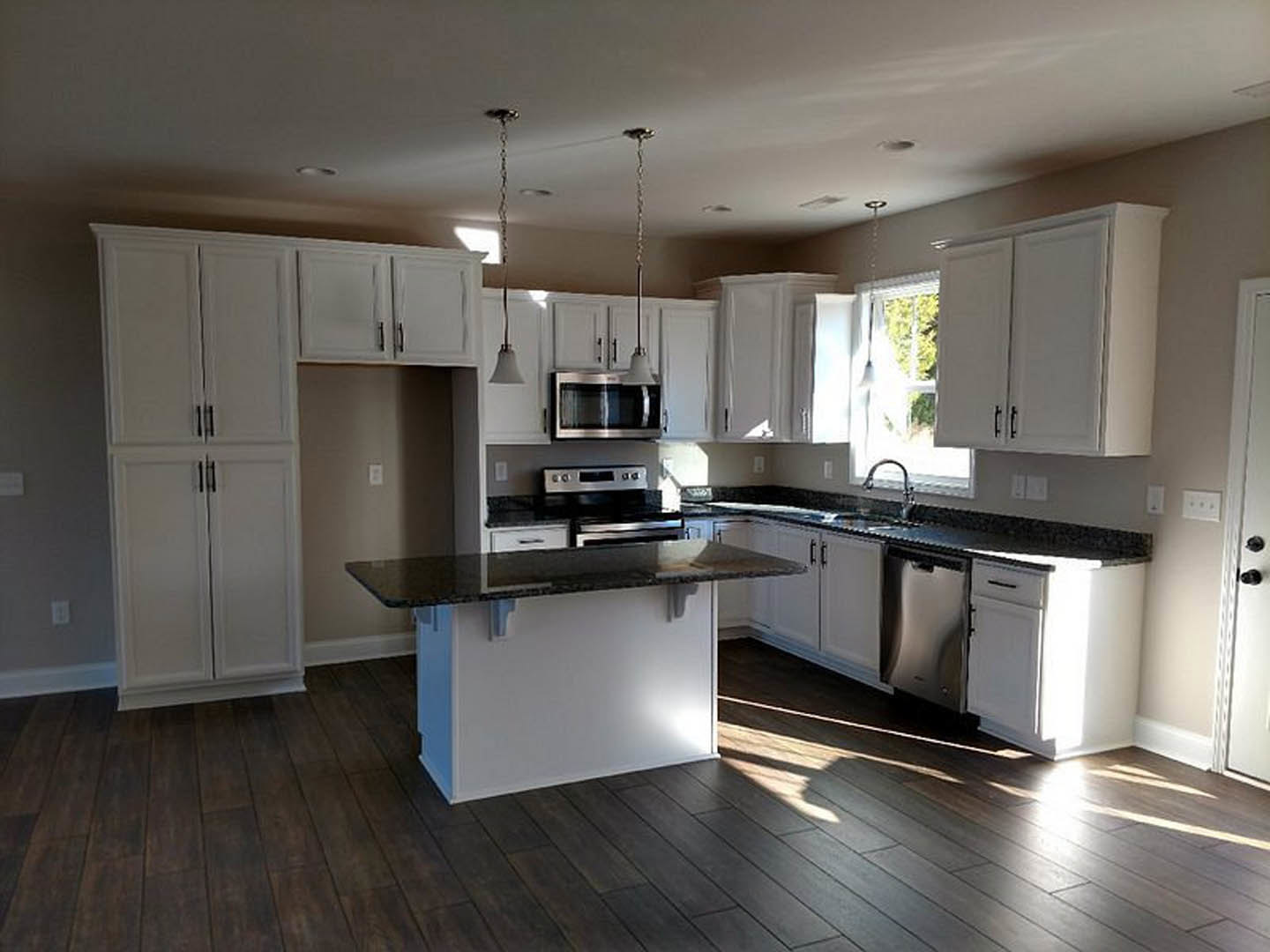 White kitchen cabinets with black granite countertops, stainless steel microwave, stove, and sink, pendant light chain hanging from ceiling, light tile flooring