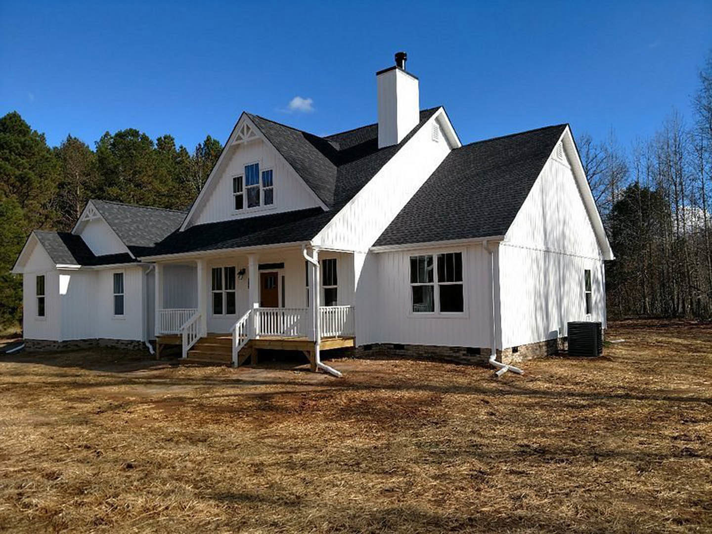 White house with black roof, white porch and railing, large windows, deck, Robert Frost Farm visible in background, blue sky with scattered clouds, surrounding trees.
