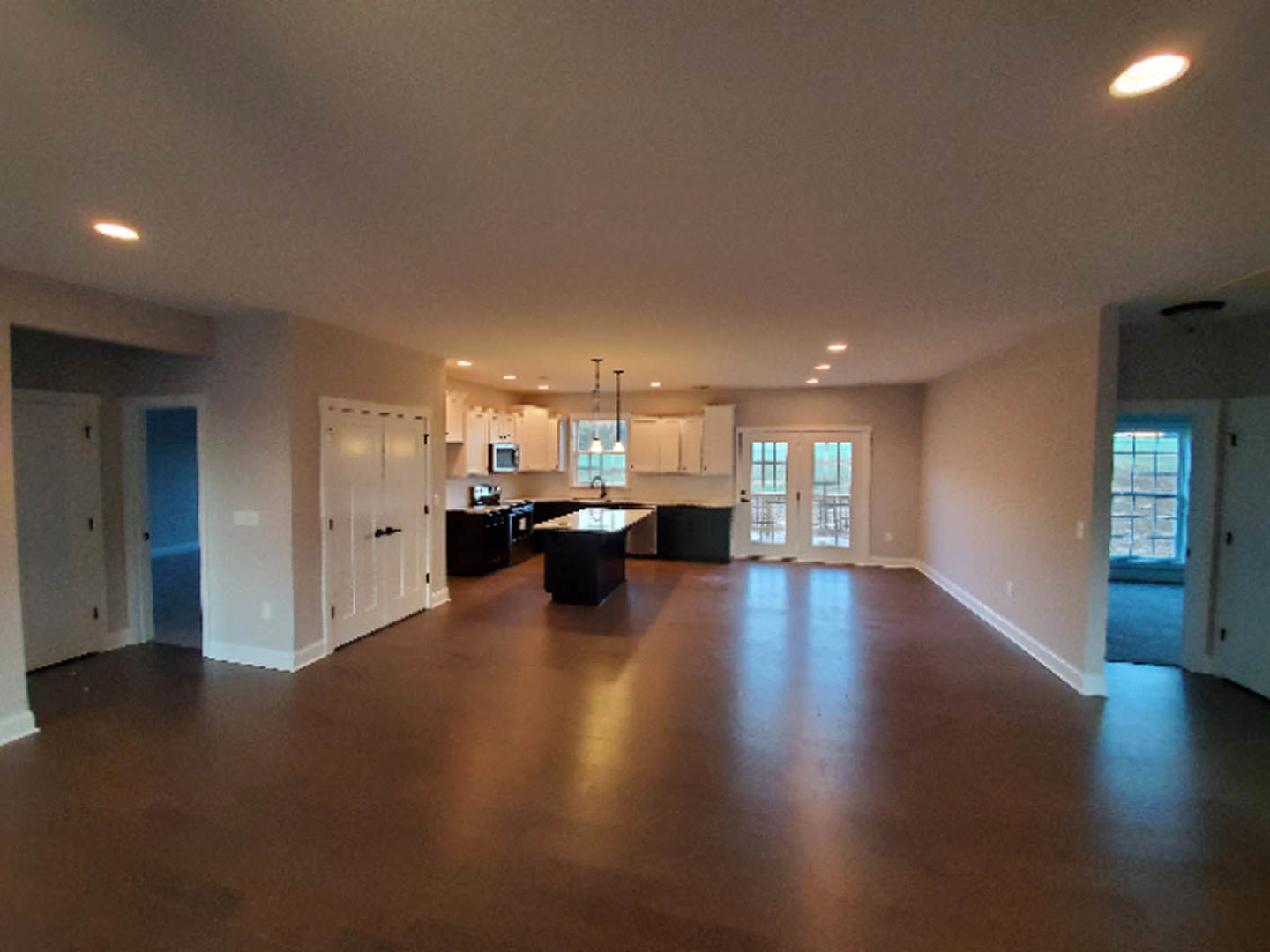 Spacious kitchen with wood flooring, central island featuring white countertop, white double doors with glass panes, recessed lighting, and adjacent dining area with table.