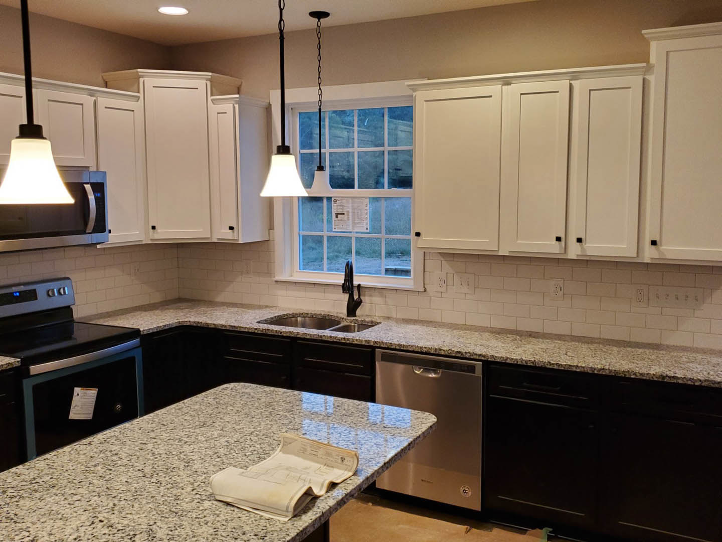 Granite countertops with white shaker cabinets, stainless steel appliances, undermount sink, pendant light fixture, and a window above the workspace