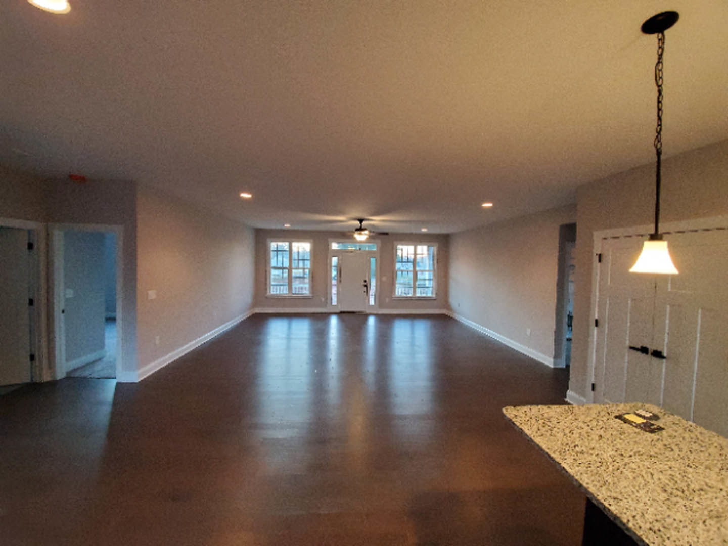 Spacious interior featuring a marble countertop, white walls, glass-paneled door, laminate flooring, ceiling light fixture, and black pole with chain