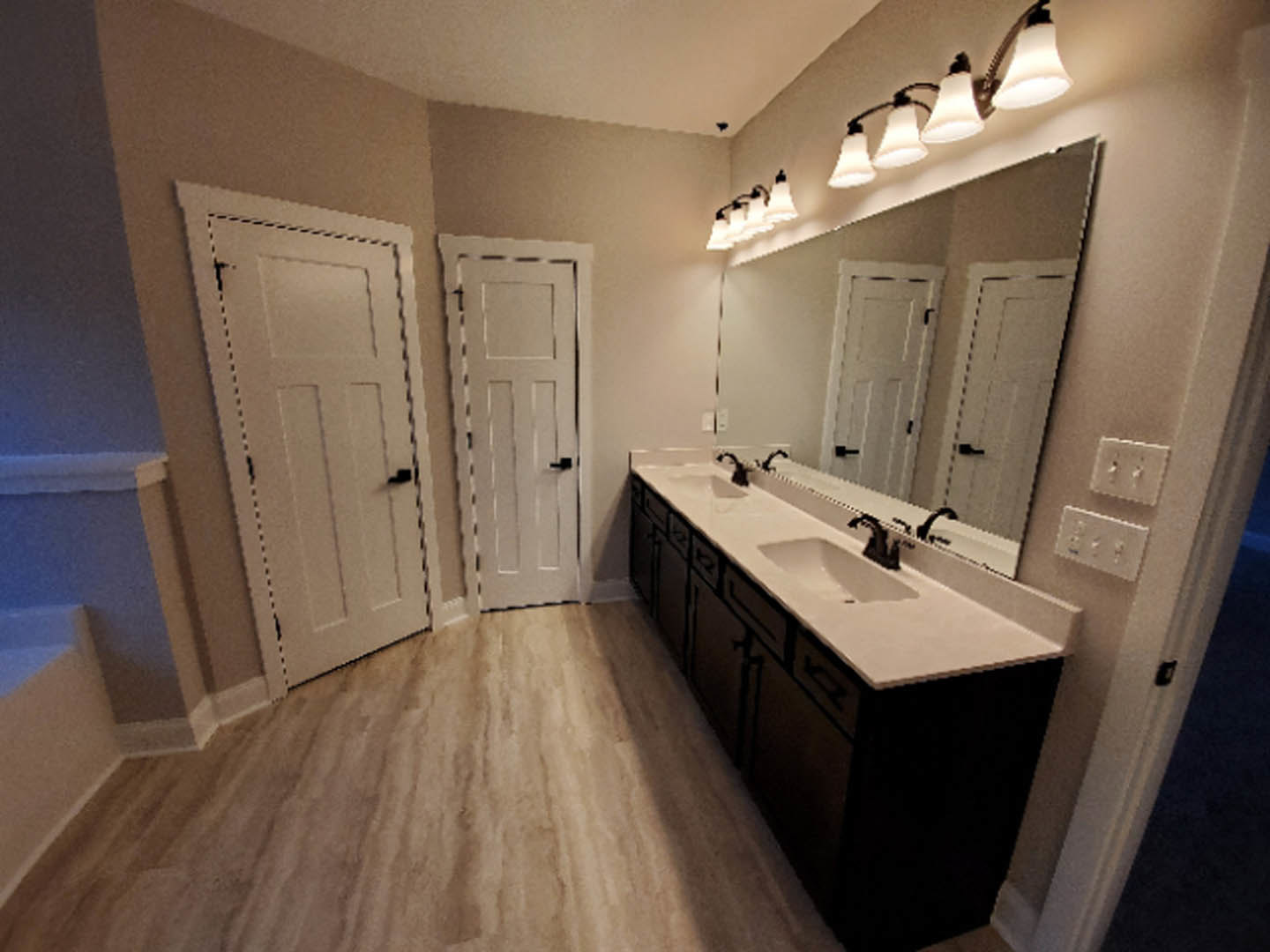 Bathroom with double vanity, white sinks, stone countertop, two paneled doors with black handles, tile flooring, wall-mounted lights above mirrors, white cabinetry