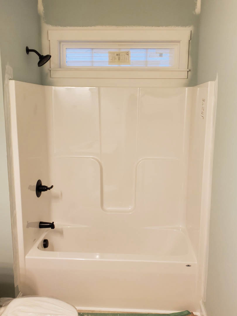 Freestanding white bathtub with black fixtures beside a window, shower head mounted on tiled wall, bright bathroom interior
