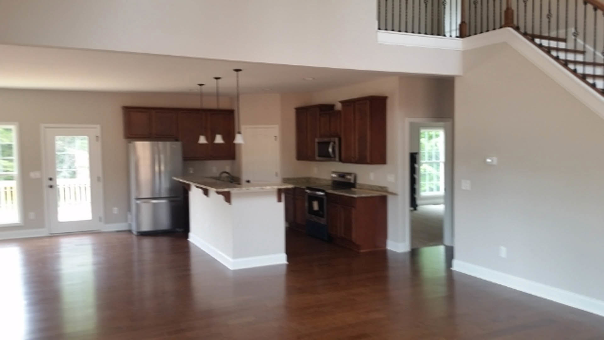 Open-concept kitchen and living room featuring hardwood floors, white kitchen island with sink, stainless steel refrigerator and microwave, white cabinetry, and glass-paneled door.
