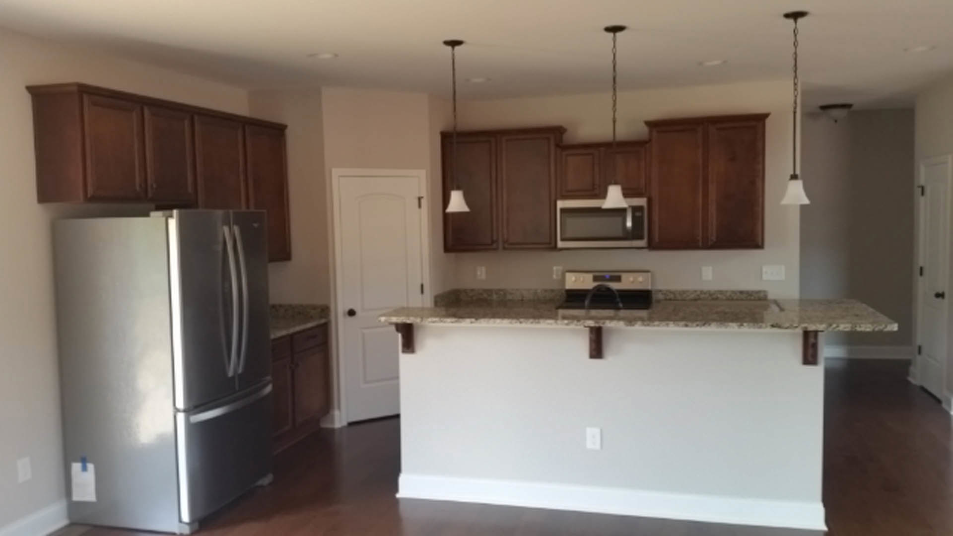 Open kitchen with marble countertop bar, stainless steel refrigerator, white cabinetry, and white walls