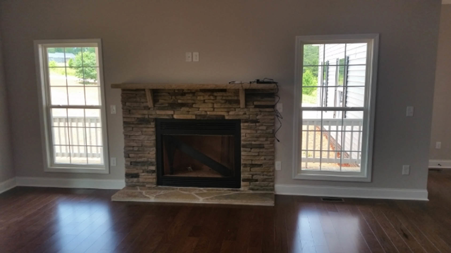 Stone fireplace with glass door set against a white wall, wood flooring, adjacent white-framed window and white door with railing