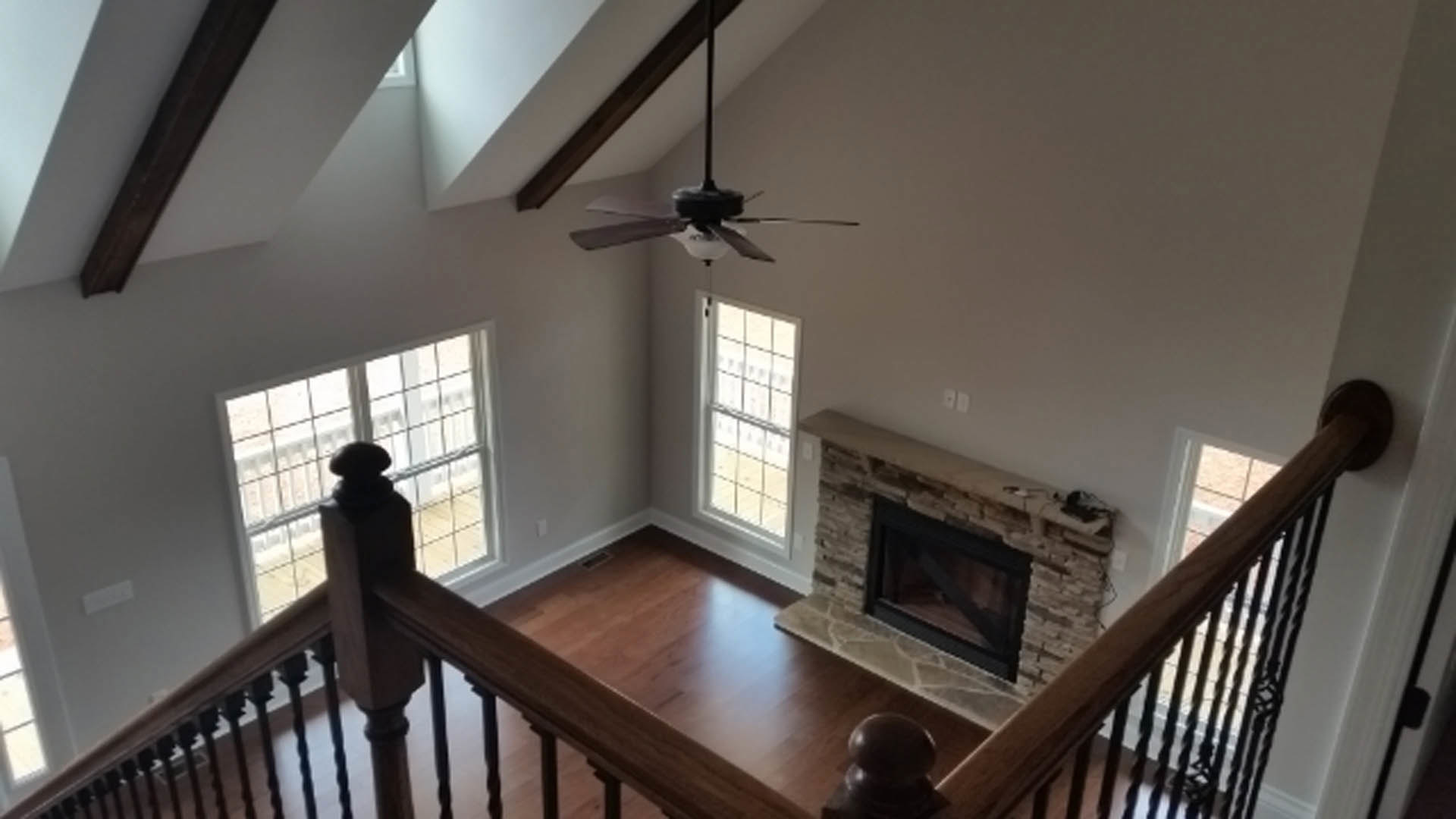 Ceiling fan mounted above wood floor, black-framed fireplace set in white wall, large window with multiple square panes, decorative molding along ceiling.