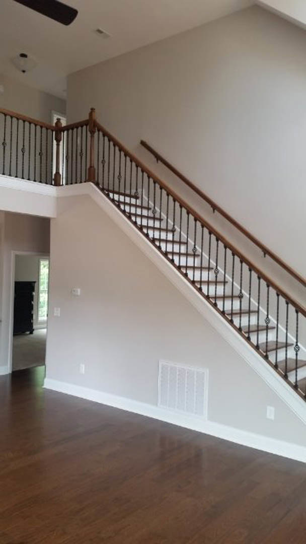 Hardwood staircase with black metal railings, white walls, and a floor vent; blurred dog’s face partially visible in foreground