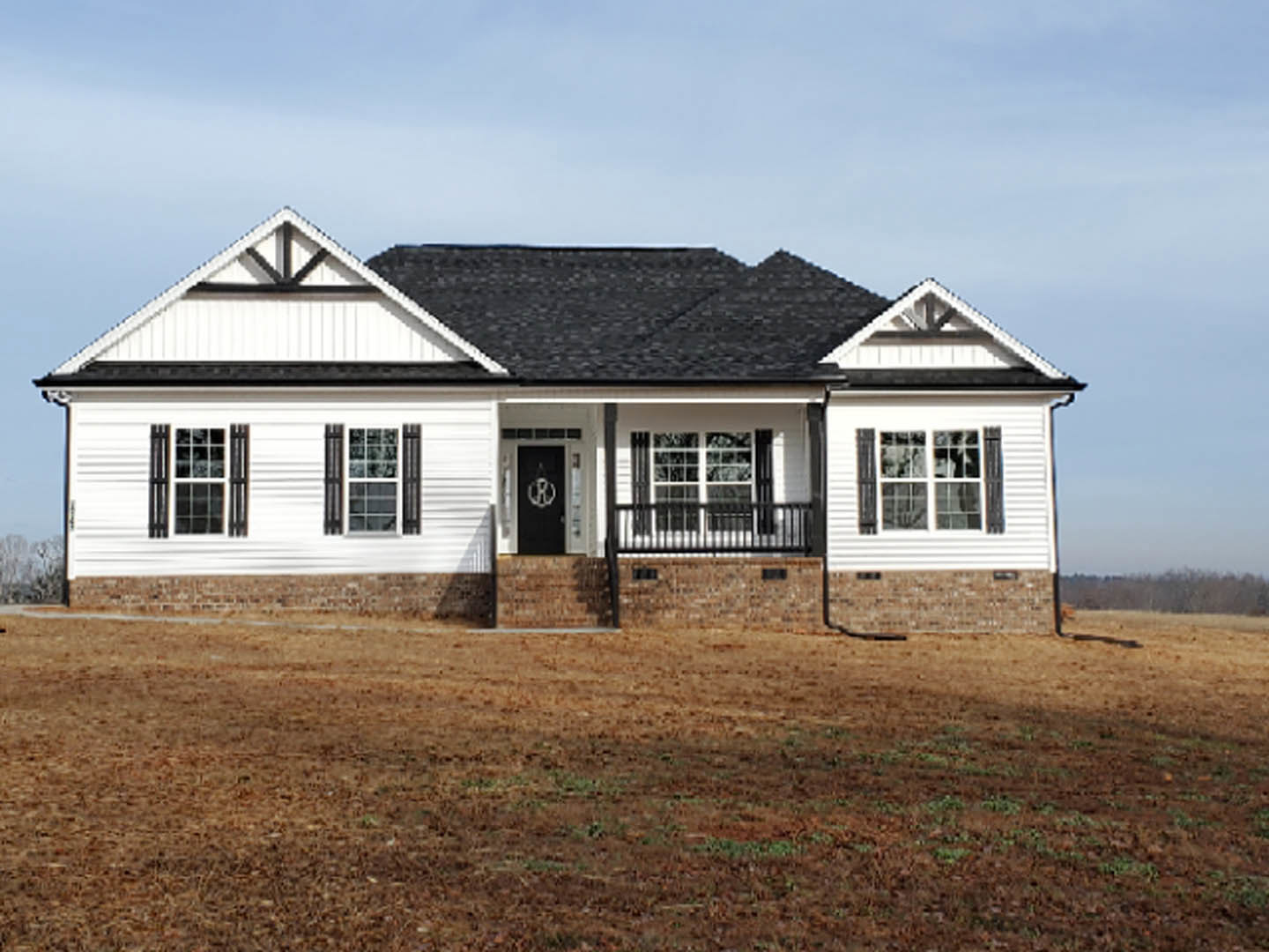 White siding house with black door and window, set beside a brown grassy field under a cloudy sky