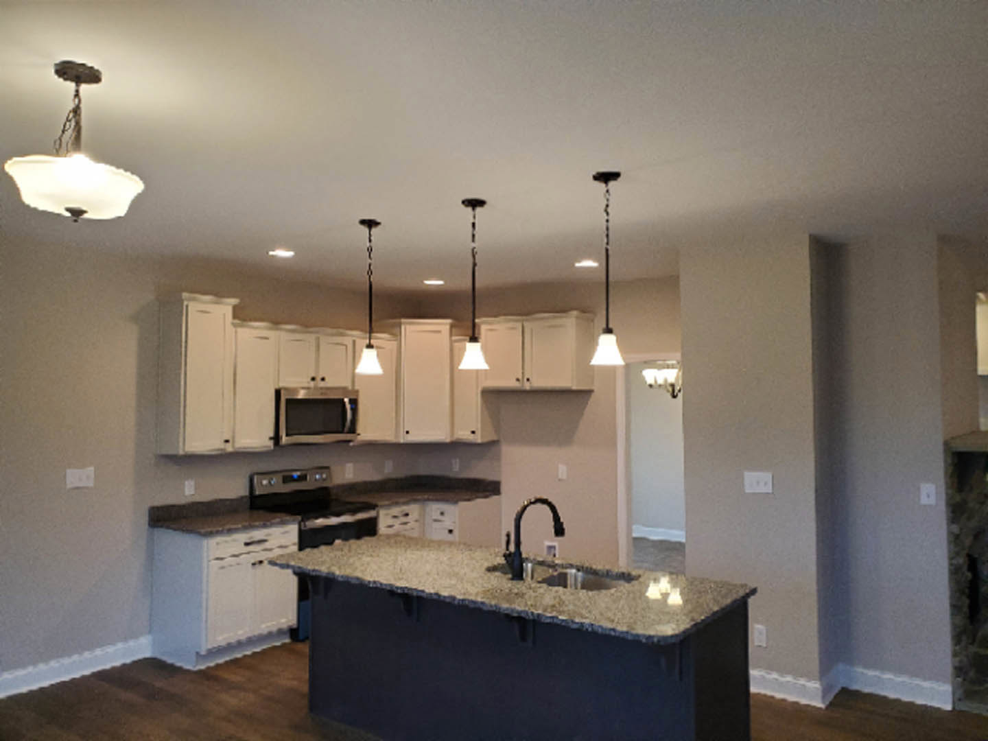 Open kitchen with large island featuring a black undermount sink, granite countertop, white cabinetry, tile backsplash, and modern light fixture with white shade.