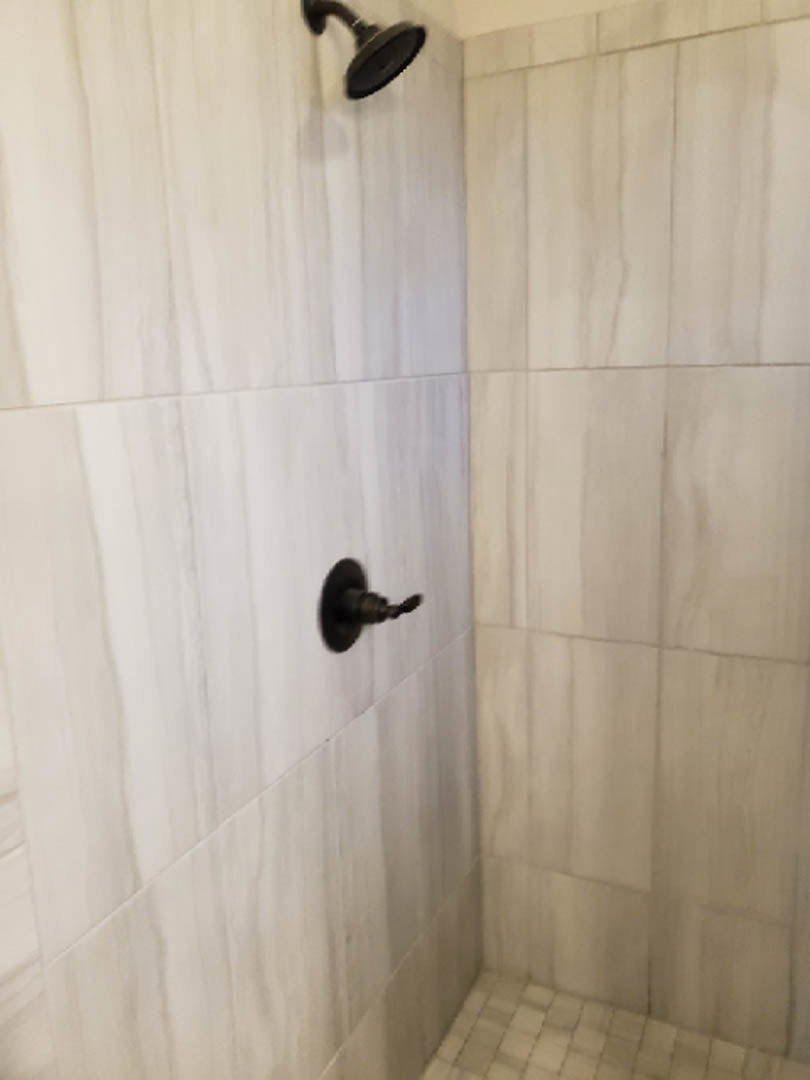 Modern tiled shower with matte black handle and fixtures, white tile walls, partial view of shower curtain.