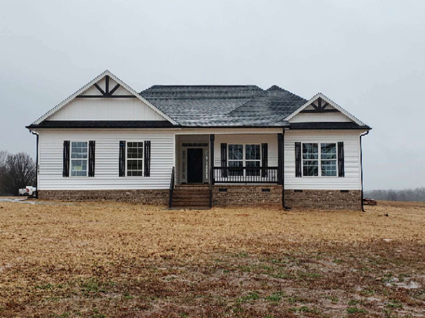 Two-story home with light siding, large windows, covered front porch, brick accent wall, and landscaped green yard