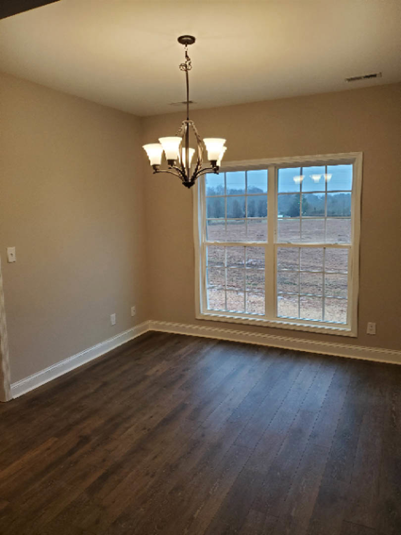 Chandelier hanging from white plaster ceiling above wood flooring, large window with field view, neutral walls