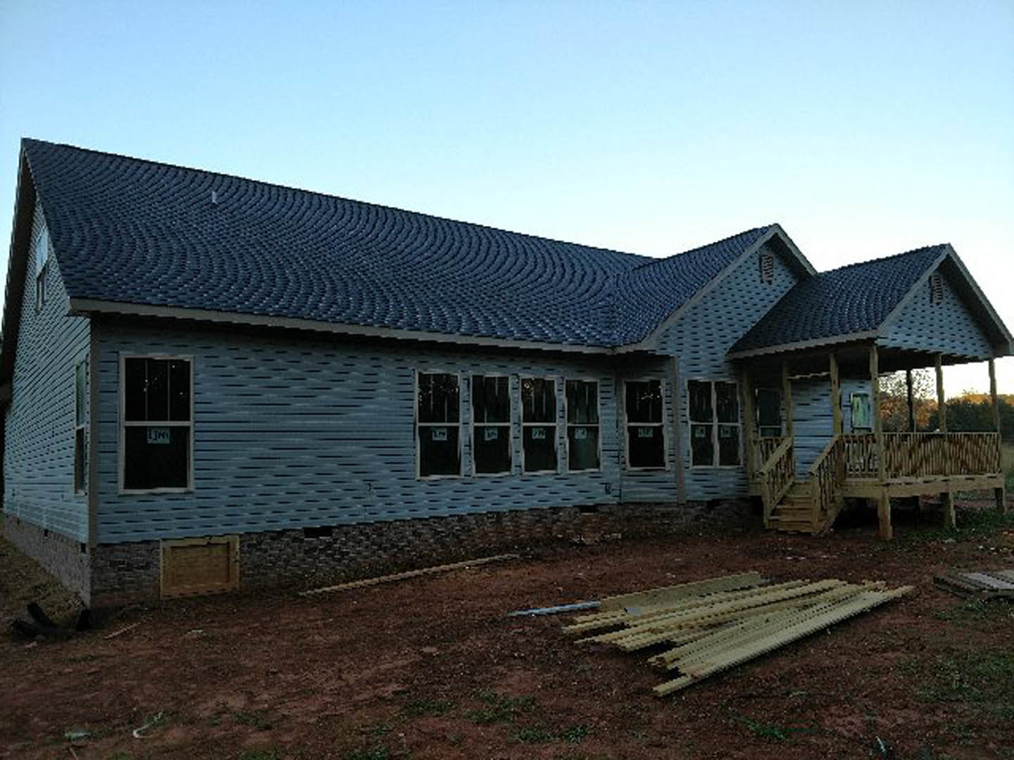 Blue house under construction with exposed siding, multiple windows, and a large pile of lumber stacked on the ground in front