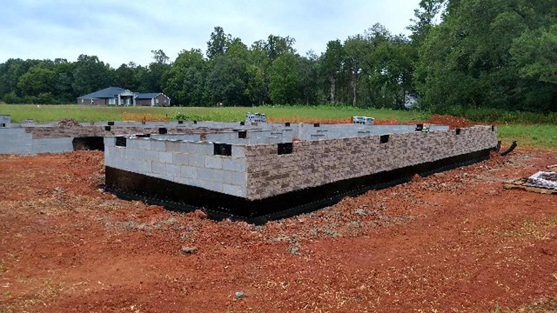 Concrete foundation with stacked stone wall, surrounded by grass and trees under a clear sky