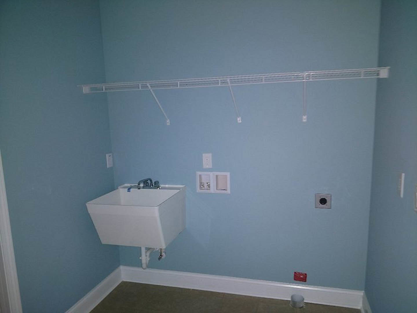 Laundry room with white cabinetry, built-in sink, wall-mounted drying rack, and light blue tile backsplash