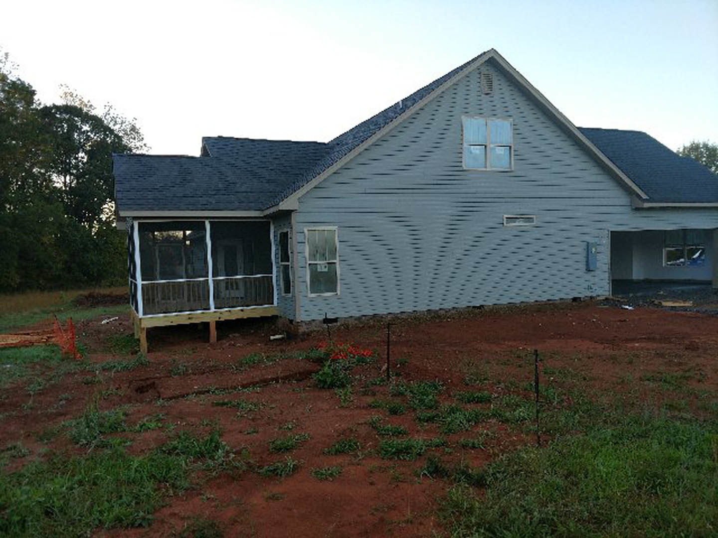 Blue siding house with two porches, screened porch, white-framed windows, red dirt yard, and flower beds