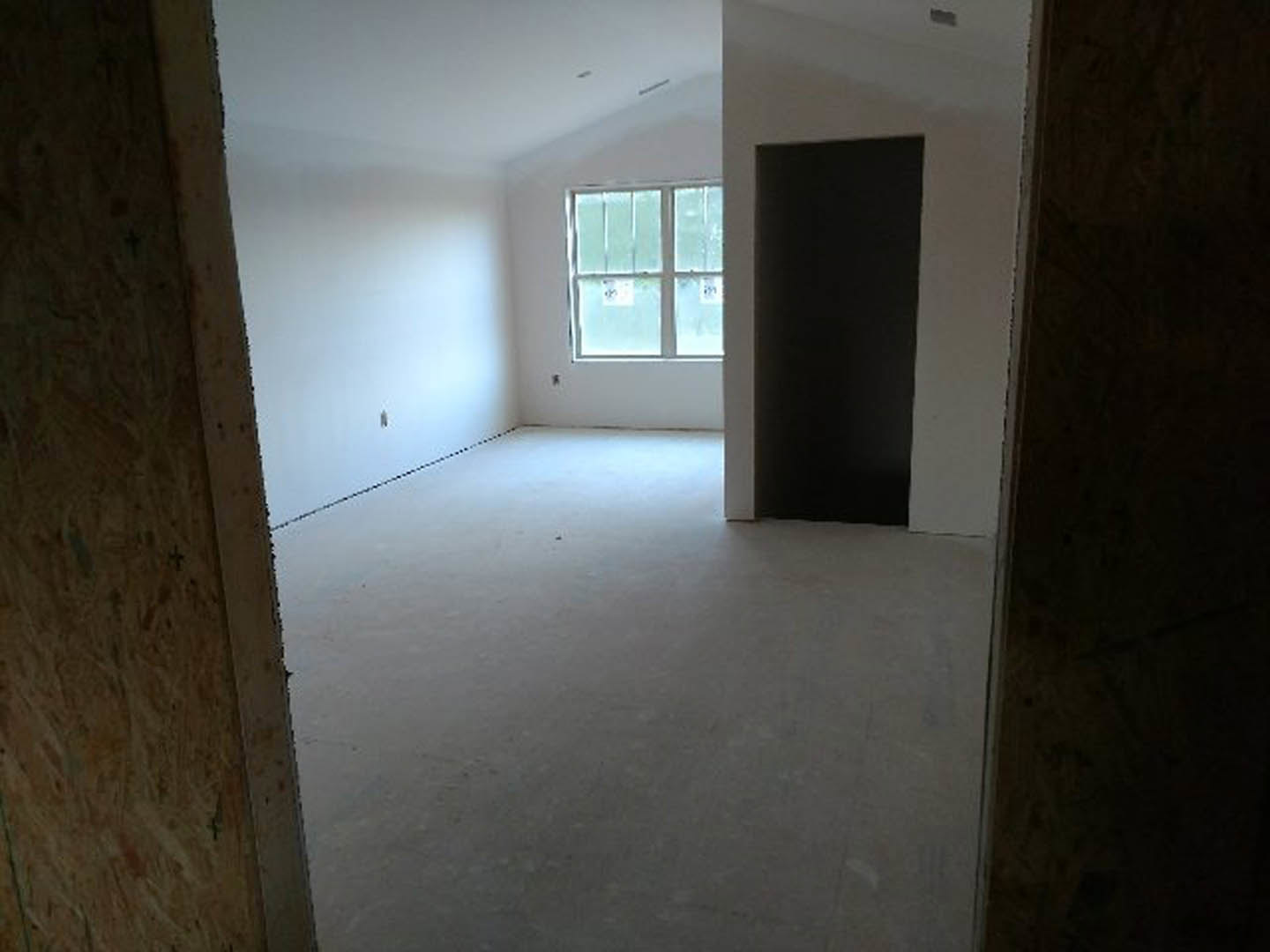 White-walled room featuring a wooden door, large window with visible signage, light-colored flooring, and black rectangular fixture with white trim