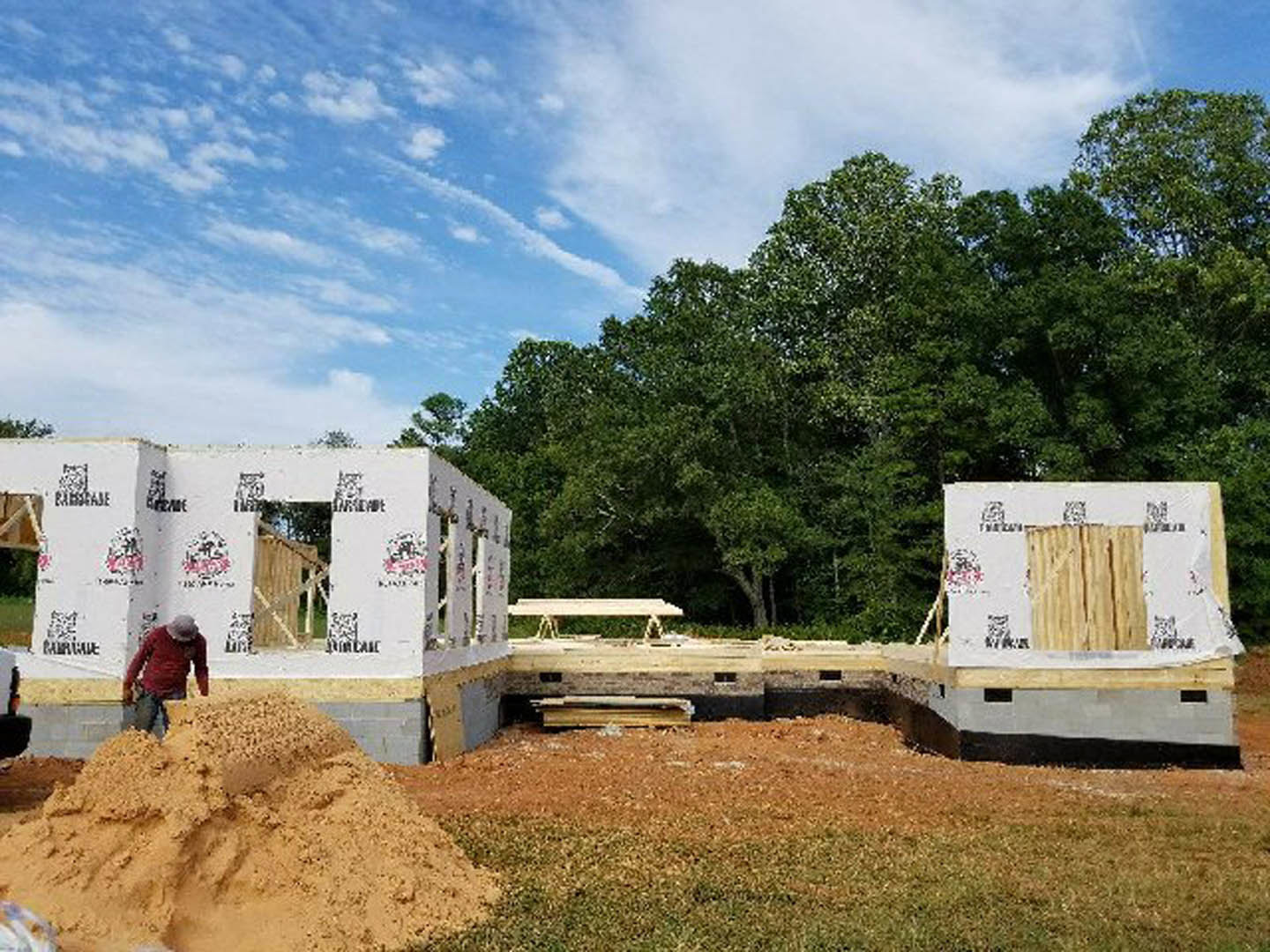 Modern two-story home with white siding, large windows, and manicured lawn; man standing near front entrance; trees and cloudy sky in background