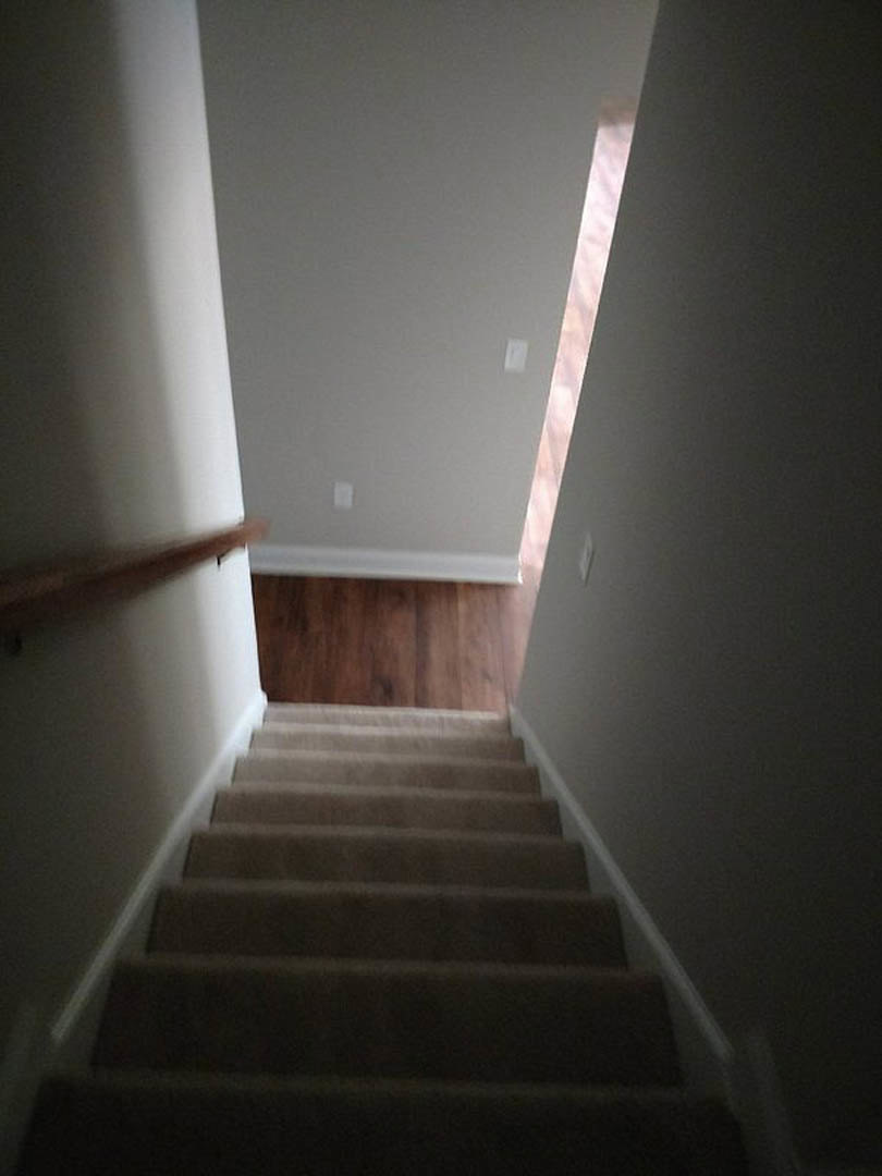 Wood staircase with metal handrail ascending toward white plaster ceiling, flanked by smooth walls in modern interior.