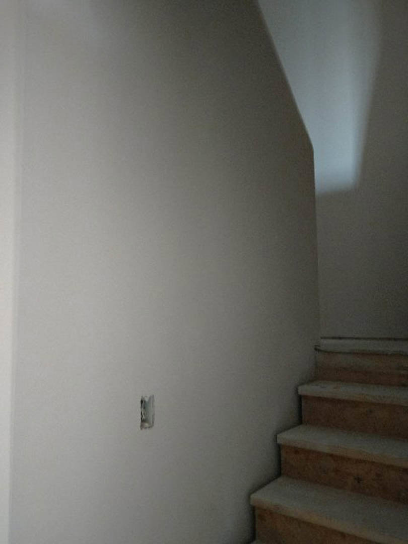 Wood staircase with metal handrail, plaster walls, recessed wall light illuminating steps, white ceiling above