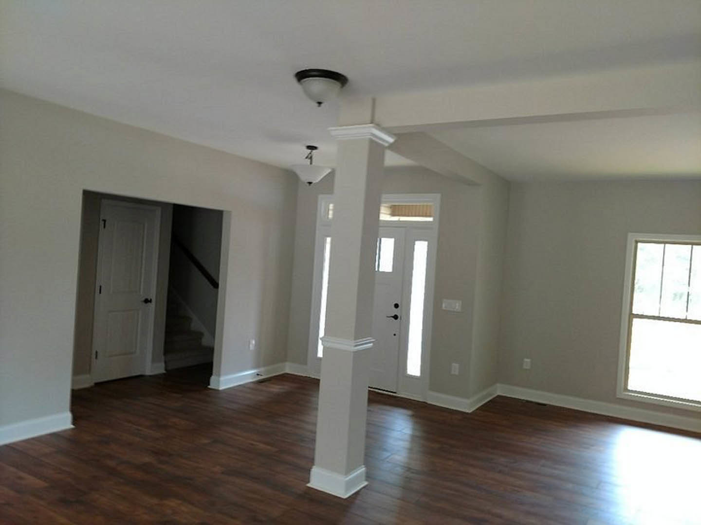 Wood flooring with white pillars, white door featuring black knobs, large window, and ceiling light fixture