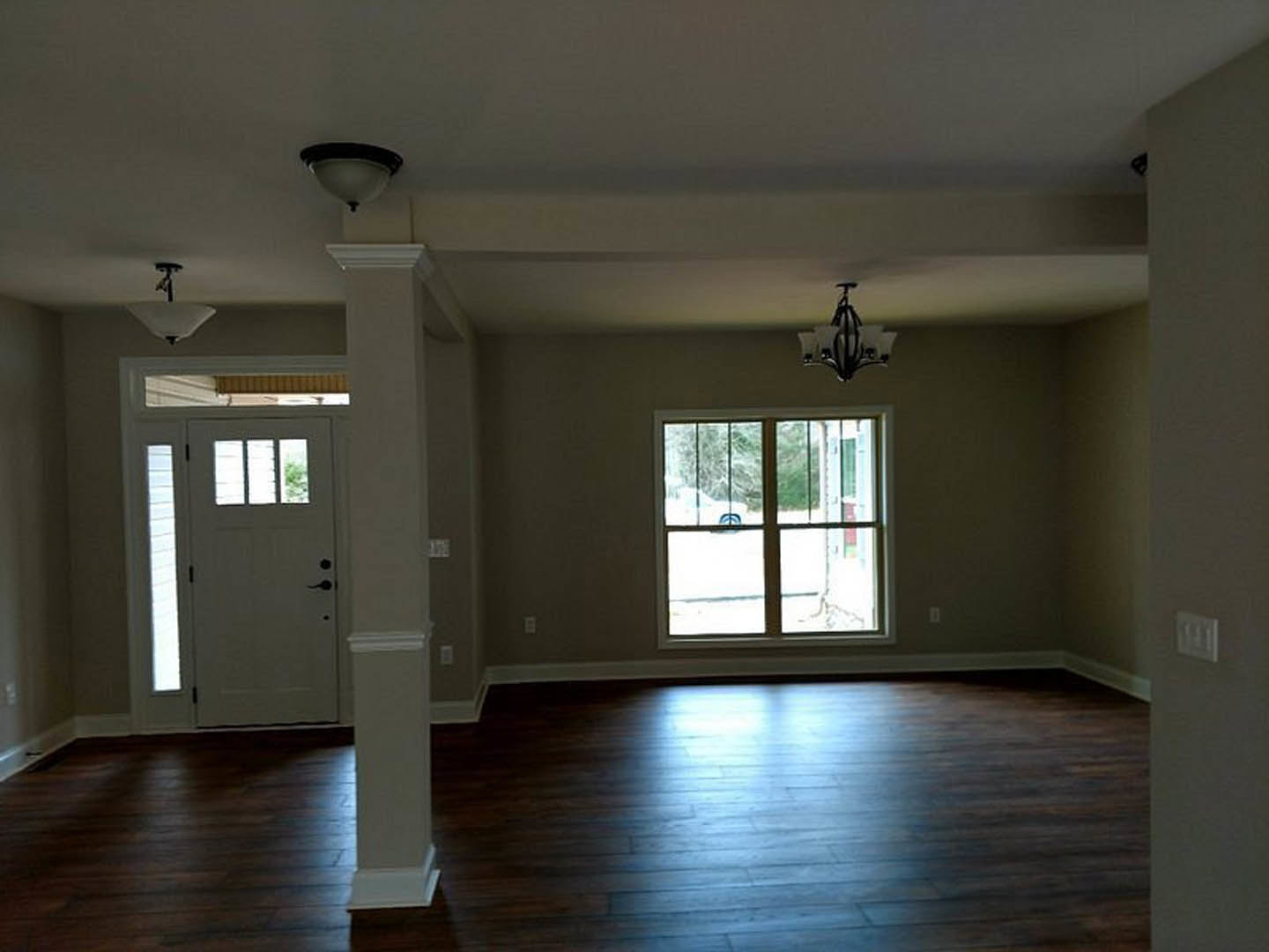 Dark wood flooring with sunlight, white walls, white door with glass panes, window showing outdoor view, chandelier overhead, white electrical outlet