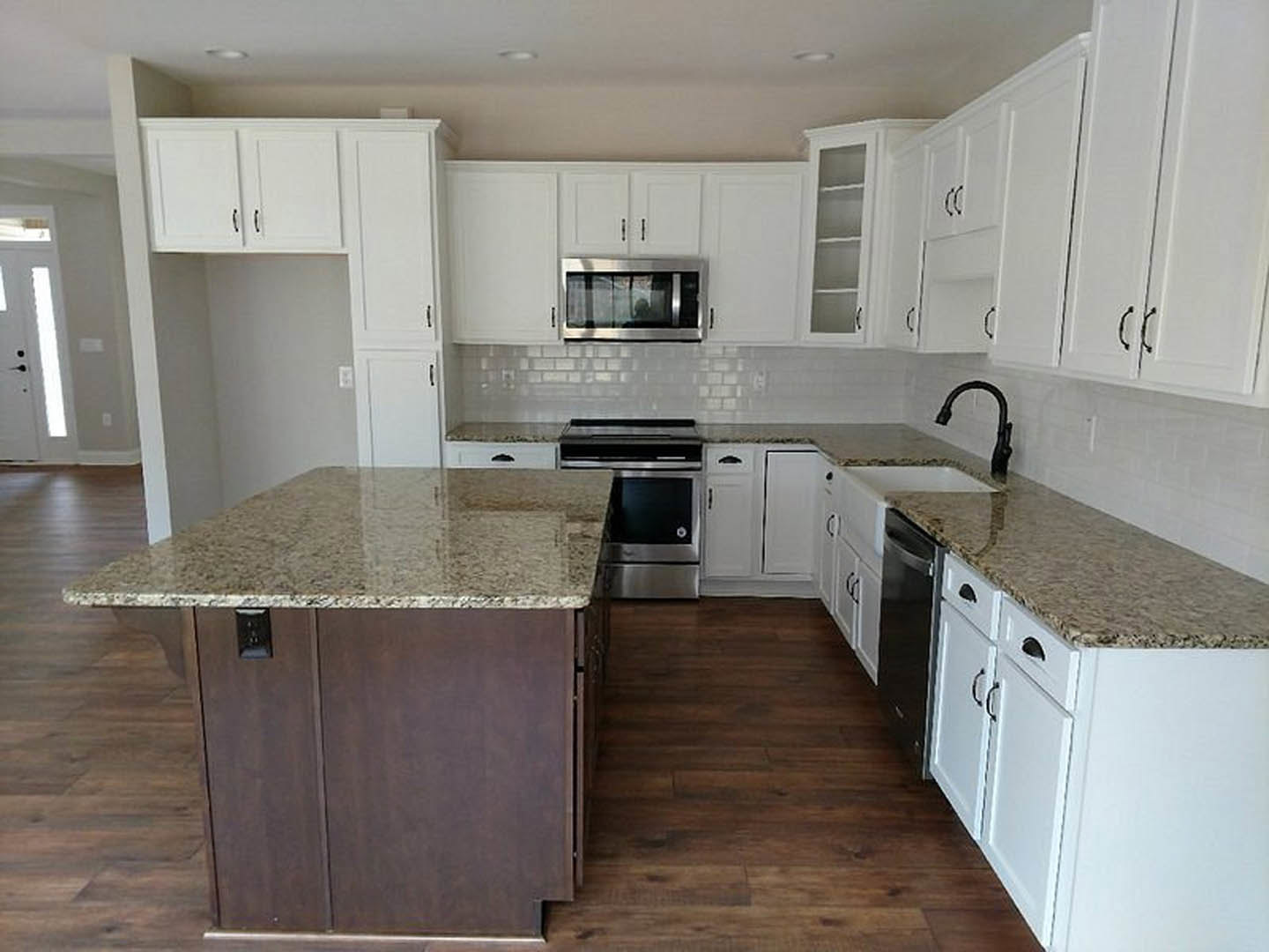 White kitchen with granite countertops, stainless steel oven, marble-topped island, black curved faucet, and open white shelving in cabinetry.