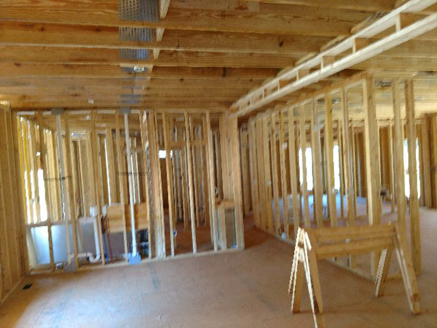 Living room with exposed wood ceiling beams, large window, hardwood floors, and wooden chair legs visible in foreground.