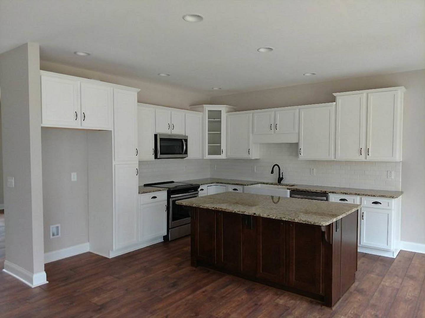 White kitchen with shaker cabinets, marble island countertop, stainless microwave, light switch on white wall, window with white trim, wood flooring