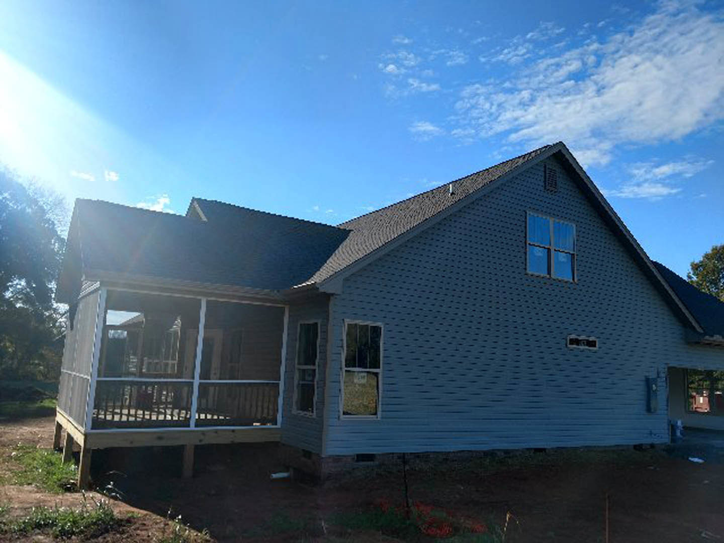 Two-story brick home with white-railed porch, large windows, and gabled roof under partly cloudy sky