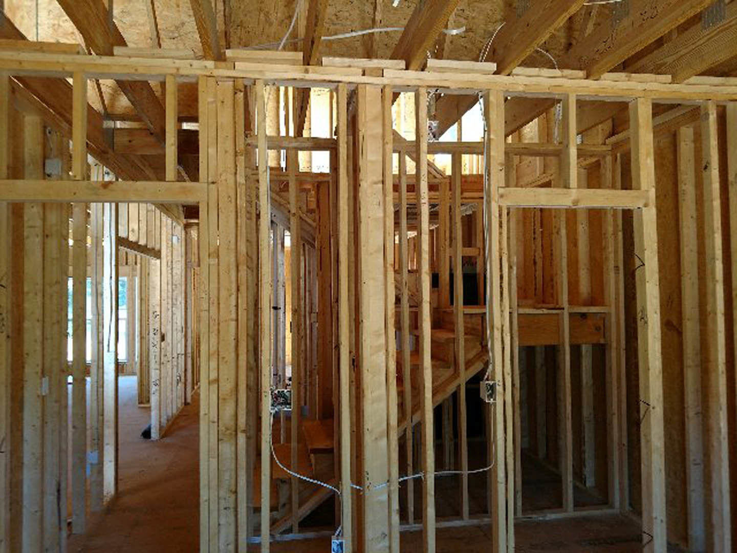 Exposed wood framing and beams inside a partially constructed house with visible insulation and lumber