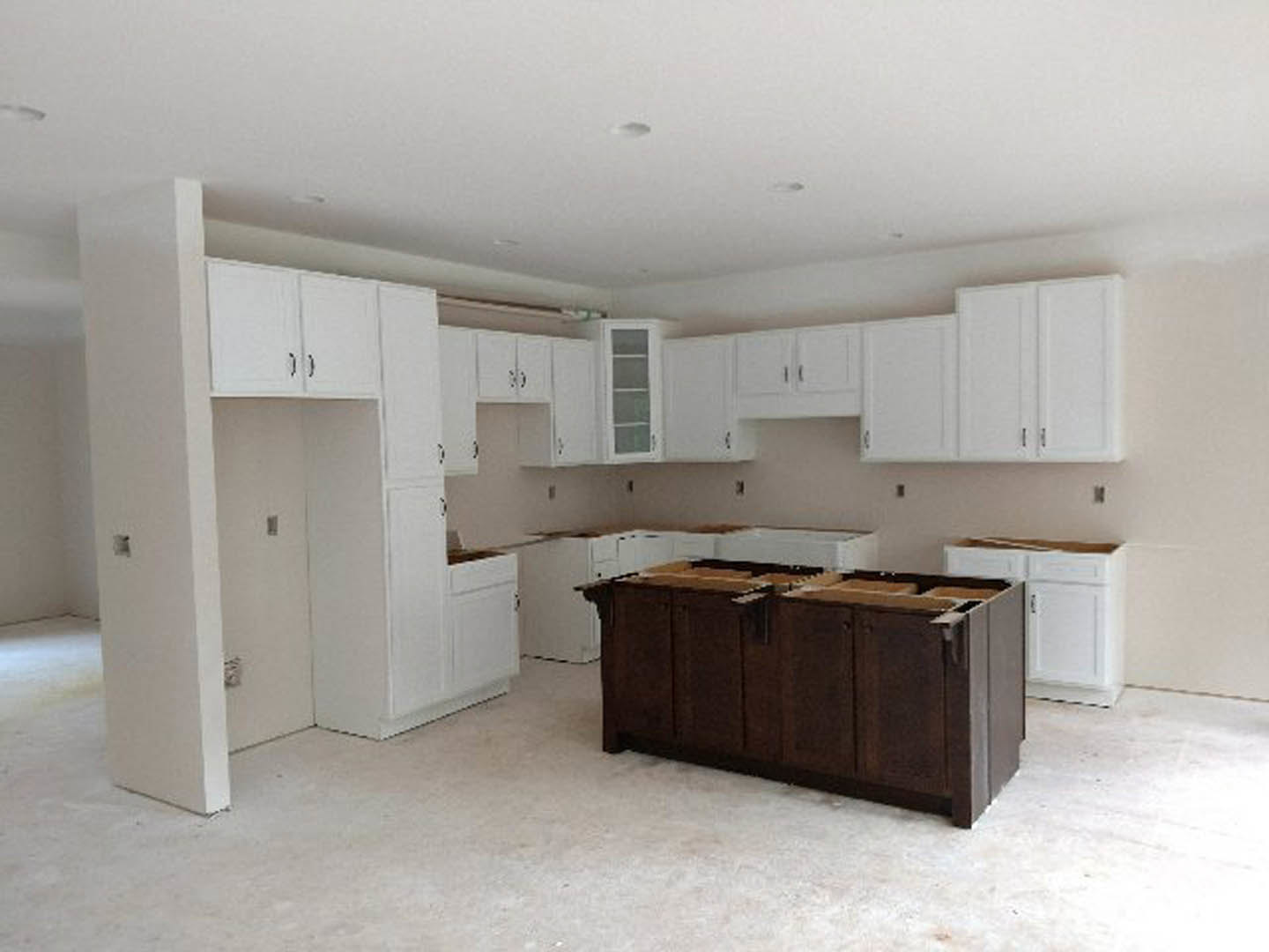 White kitchen cabinets with silver hardware, brown wood island with quartz countertop, stainless steel sink, light switch on white wall, window with white frame, hardwood flooring