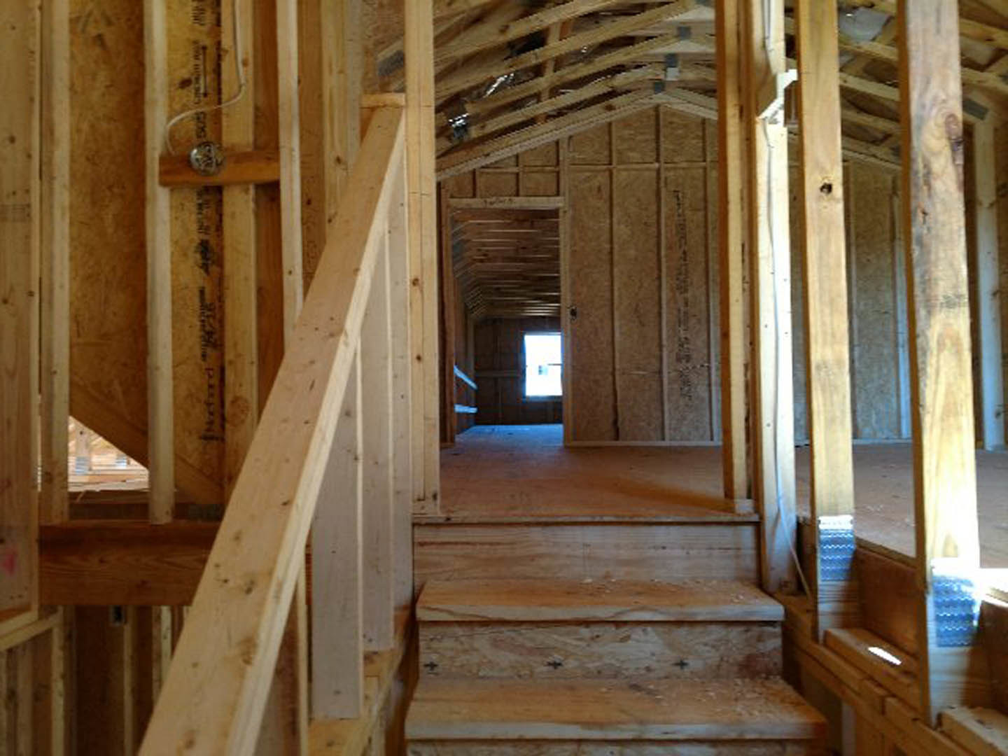 Hardwood staircase with wooden railing, exposed ceiling beams, wood-paneled walls, and a window letting in natural light